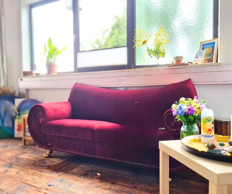 Rotes Samtsofa mit gebogenen Armlehnen in einem hellen Seminarraum mit großen Fenstern und Holzboden.